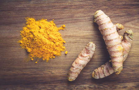 Turmeric root and spice powder on a wooden cutting board. Top viewの写真素材