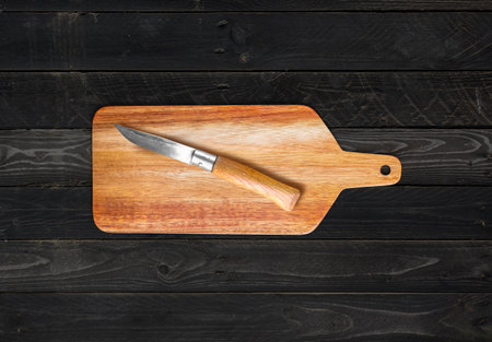 Wooden cutting board and pocket knife on black wood table background