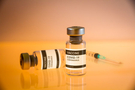 Covid-19 vaccine bottle and syringe on a yellow laboratory backgroundの写真素材