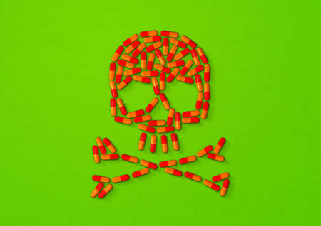Skull made of orange capsule pills isolated on green background. 3D illustrationの写真素材