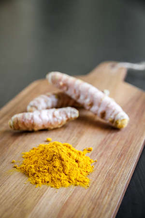 Turmeric root and spice powder on a wooden cutting boardの写真素材