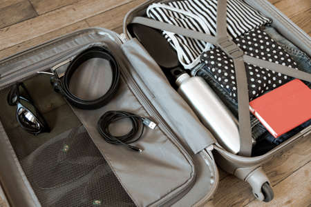 Open travel suitcase full of clothes isolated on wooden backgroundの写真素材