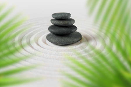 Black stones pile in the sand behind palm leaves. Zen japanese gardenの写真素材