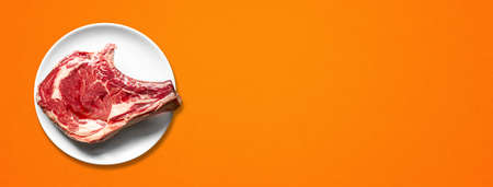 Raw beef prime rib and plate isolated on orange background. Top view. Horizontal banner