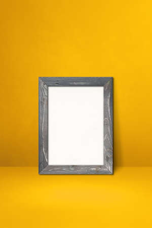 Wooden picture frame leaning on a yellow wall. Blank mockup template