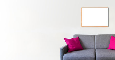 Empty wooden picture frame on a white wall above a sofa. Minimalist interior background. Horizontal bannerの写真素材