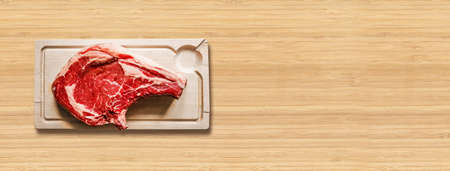 Raw beef prime rib and wooden cutting board isolated on wooden background. Top view. Horizontal bannerの写真素材
