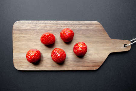 Strawberries on a wooden cutting board. Black background. Top viewの写真素材
