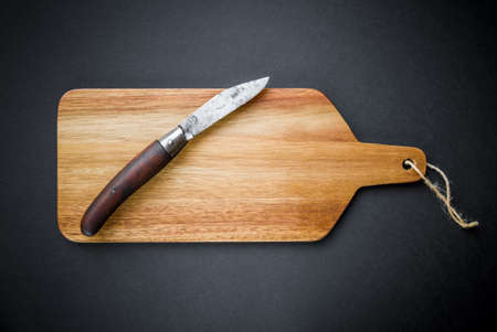 Traditional pocket knife on a wooden cutting board. Black background