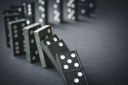Black dominoes chain on a dark table background. Domino effect conceptの写真素材
