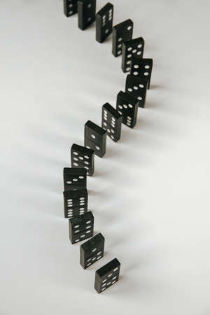 Black dominoes chain on a white table background. Domino effect conceptの写真素材