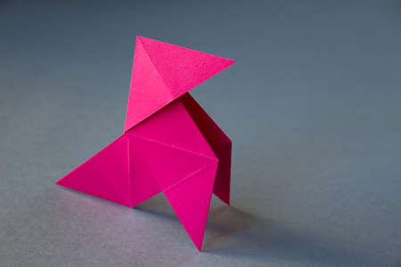 Pink paper hen origami isolated on a blank grey background. Cocotte en papier