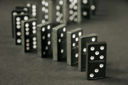 Black dominoes chain on a dark table background. Domino effect conceptの写真素材