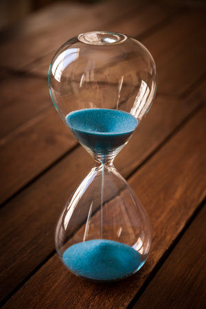 Hourglass containing blue sand on a rustic wooden board background