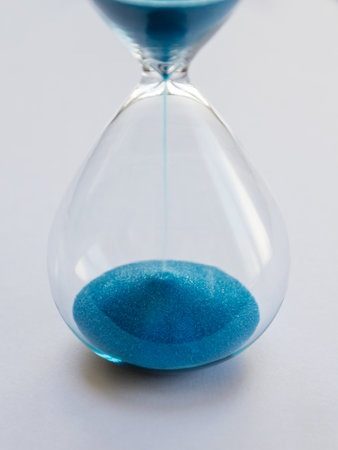 Hourglass containing blue sand isolated on white background. Concept of time passing