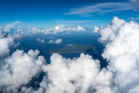 Makatea Island emerges from the vast Pacific Ocean, partially hidden by thick white clouds. The...