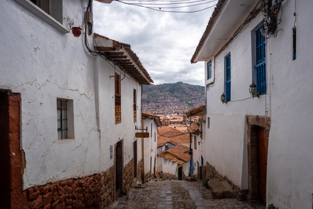 A picturesque stone-paved street in San Blas, Cusco, features colonial whitewashed houses, blue doors, potted flowers, and a steep stairway leading to artisan shops. Peruの写真素材