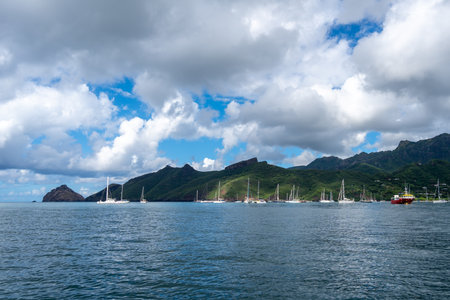 Taiohae Bay in Nuku Hiva, Marquesas Islands, features a serene harbor with anchored sailboats, lush green mountains, and a deep blue Pacific Ocean under a bright sky. French Polynesiaの写真素材