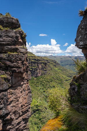 Green mountain ridges and steep rocky cliffs surround the Waqrapukara archaeological site, offering breathtaking panoramic views of the Andean landscape under a clear blue skyの写真素材