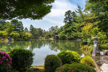 Kenroku-en Garden in Kanazawa blends natural beauty and harmony with its pond, stone lantern, and lush vegetation, creating a peaceful atmosphereの写真素材