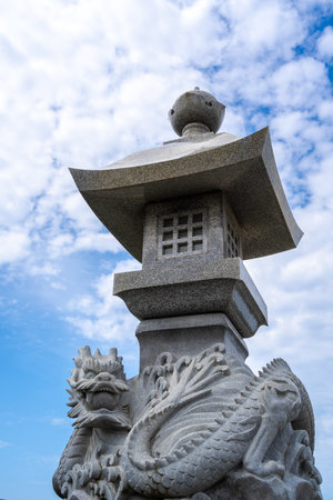 Ornate stone lantern featuring a dragon sculpture stands under a bright sky in Enoshima island, Japan, blending mythical artistry with traditional designの写真素材