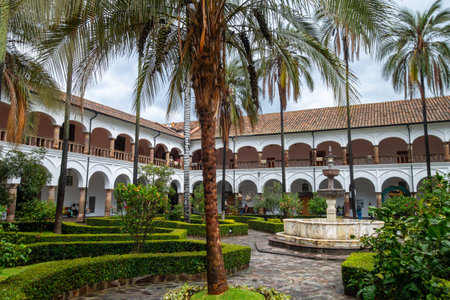 Historic convent and church courtyard in Quito, Ecuador, featuring colonial architecture, palm trees, and a tranquil fountainの写真素材