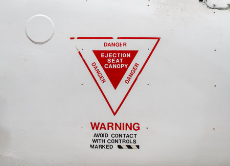 A close-up of an aircraft fuselage featuring a red and white triangular warning for an ejection seat canopy and safety instructions belowの写真素材
