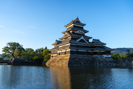Matsumoto Castle stands majestically as golden light reflects off its dark wooden exterior and calm surrounding waters in Matsumoto, Japanの写真素材