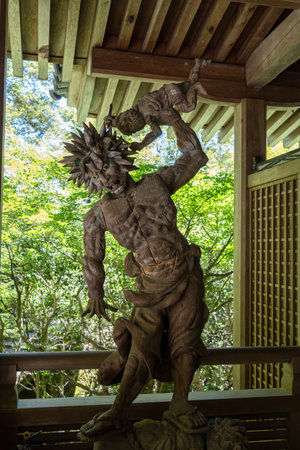 Intricately carved wooden Oni demon statue at Mitaki-Dera temple in Hiroshima, portraying fierce expression and dynamic pose under a traditional wooden roofの写真素材