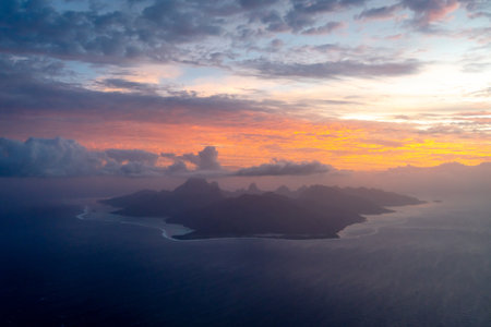 Moorea island, seen from above during sunset, reveals its rugged peaks, surrounding lagoon, and dramatic coastline, bathed in warm golden and blue huesの写真素材