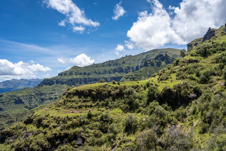 The Waqrapukara site in Peru features dramatic rock formations, green valleys, and steep cliffs, offering breathtaking views of the Andean highlands under a bright blue skyの写真素材