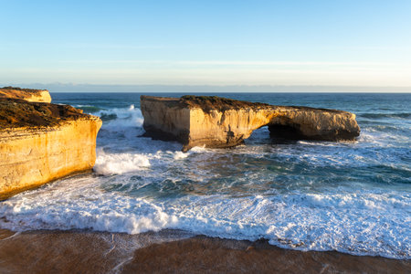 Golden light illuminates London Bridge, a famous rock formation at the Twelve Apostles site along...