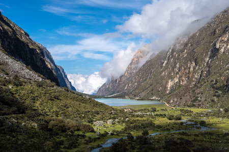 A lush green valley stretches between towering mountains, with a winding river leading to a tranquil lake. This breathtaking scenery is part of the Laguna 69 trek in Huaraz, Peruの写真素材