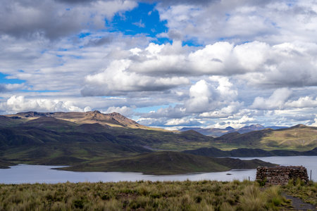 Lake Lagunillas in Peru is surrounded by rolling hills and grasslands, with dark storm clouds above and a distant rain shower falling over the mountainsの写真素材