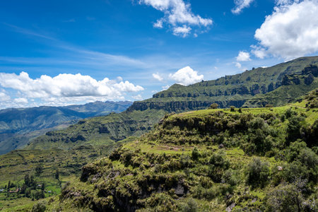 The Waqrapukara site in Peru features dramatic rock formations, green valleys, and steep cliffs, offering breathtaking views of the Andean highlands under a bright blue skyの写真素材