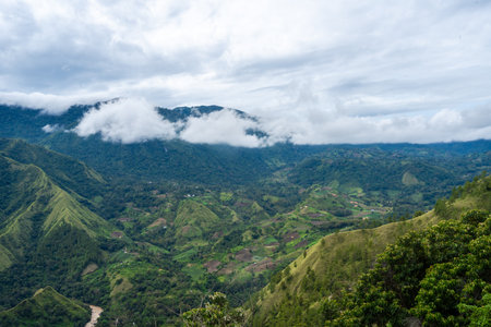 Lush green mountains stretch across the Toraja region in Sulawesi, Indonesia, under a cloudy sky with mist clinging to the ridgelinesの写真素材