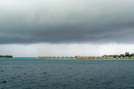 A scenic view of luxury overwater bungalows on motus around Bora Bora, with stunning turquoise waters and dramatic clouds aboveの写真素材