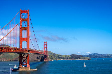 The Golden Gate Bridge stretches across the bay, its red towers contrasting against the blue sky and...
