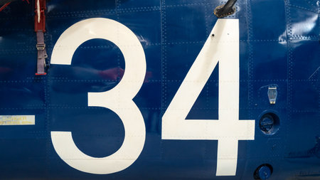Close-up of an old aircraft fuselage painted deep blue with a large white number 34, riveted metal panels, and various mechanical elementsの写真素材