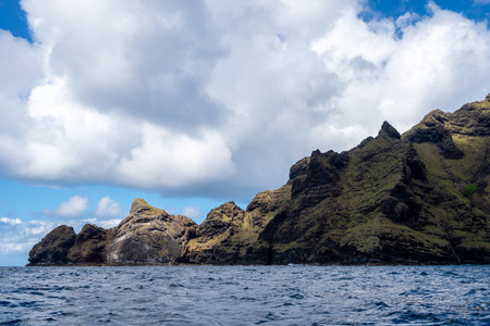 Green cliffs rise above the ocean along the rugged coastline between Taiohae and Hakaui, Nuku Hiva, Marquesas Islands, French Polynesia, under a cloudy skyの写真素材