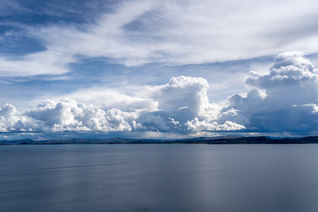 Expansive view of Lake Titicaca from Taquile Island, with calm waters reflecting a dramatic sky filled with billowing white and blue cloudsの写真素材