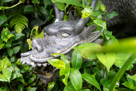 A bronze dragon fountain emerges from lush green foliage on Enoshima Island, Japan, with water flowing gently from its open mouthの写真素材