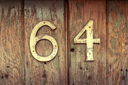 The house number 64 appears on a worn wooden surface with peeling paint and rusted screws. The aged texture and faded colors add a rustic, vintage feel to the scene, emphasizing the passage of time and weathering effectsの写真素材