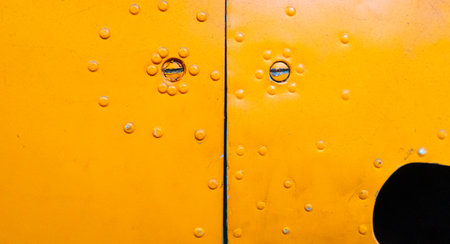 Detail of an old aircraft fuselage painted yellow, showing rivets, screws, and a narrow gap between...
