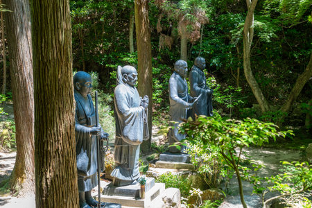 Tall bronze statues of monks stand solemnly in the forested grounds of Mitaki-Dera temple in...