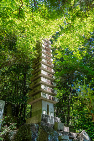 A tall stone pagoda rises through the forest canopy at Mitaki-Dera temple in Hiroshima, surrounded by vivid green foliage and natural lightの写真素材