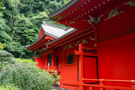 Bright red main hall of Enoshima-Shrine Nakatsunomiya stands surrounded by trees, traditional lanterns, and guardian statues on Enoshima Island, Japanの写真素材