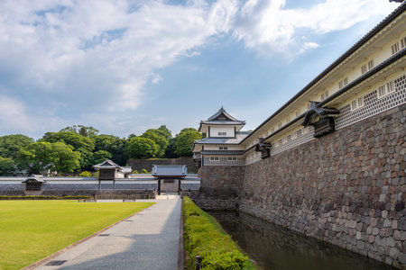 Traditional Japanese architecture of Kanazawa Castle with stone walls and a moat, surrounded by greenery and blue sky in Japanの写真素材