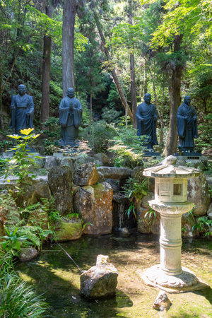 Tall bronze statues of monks stand solemnly in the forested grounds of Mitaki-Dera temple in Hiroshima, radiating peace and reverenceの写真素材