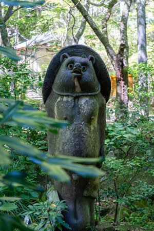 A whimsical tanuki statue stands amid lush foliage at Mitaki-Dera Temple in Hiroshima, blending folklore charm with the tranquility of natureの写真素材